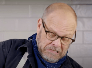Alton Brown making a grimacing face while wrangling his mixer
